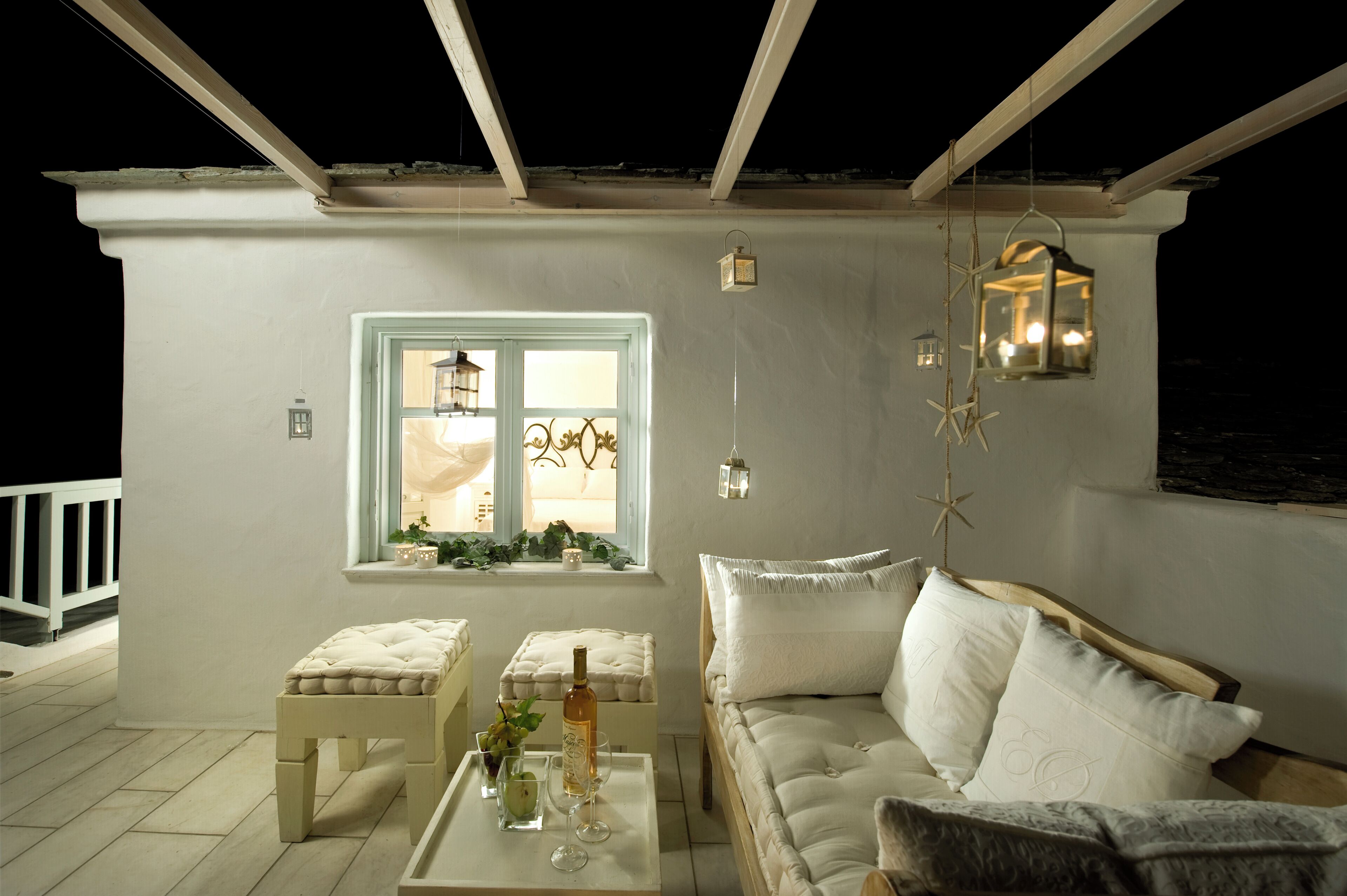 Une pièce chaleureuse avec un canapé blanc, une petite table sur laquelle se trouvent une bouteille et des verres, une fenêtre donnant sur un beau paysage et des lampes décoratives suspendues au plafond.