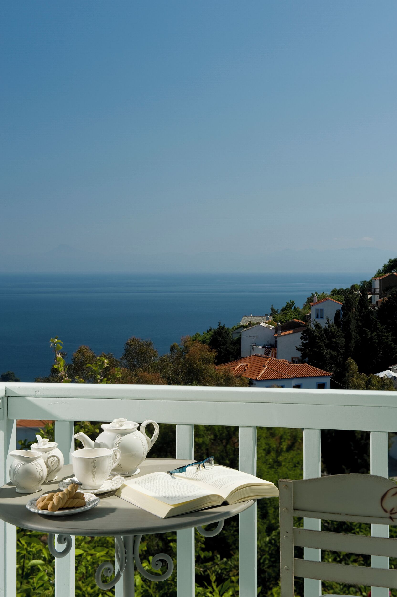 Une table avec un service à thé et des biscuits, placée sur un balcon donnant sur la mer.