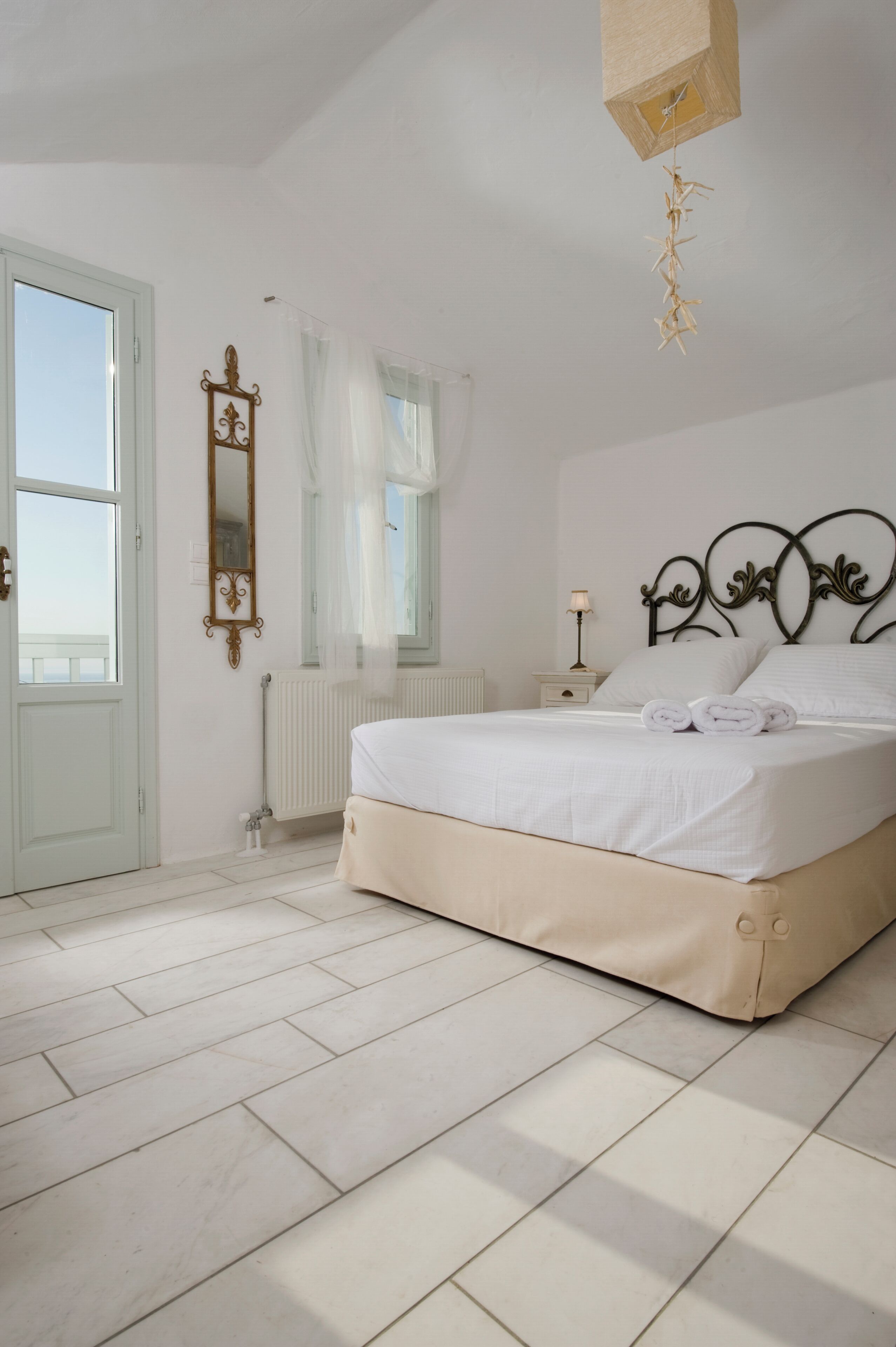 Ein Schlafzimmer mit Bett, Nachttisch, Spiegel, Heizkörper und einem Fenster mit Vorhängen.