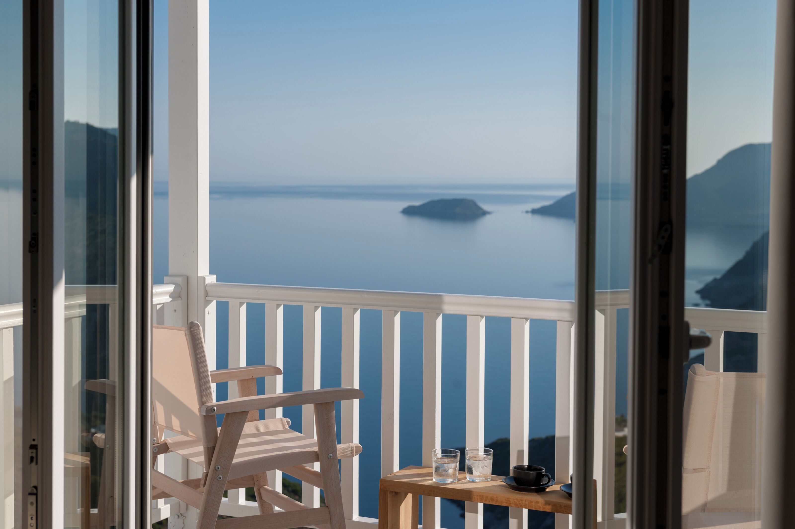 A balcony with a white railing, a wooden chair, and a small table with a glass and a cup.