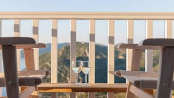 Dos sillas de madera con una mesa entre ellas, sosteniendo dos copas de vino blanco, con vistas a un paisaje montañoso.