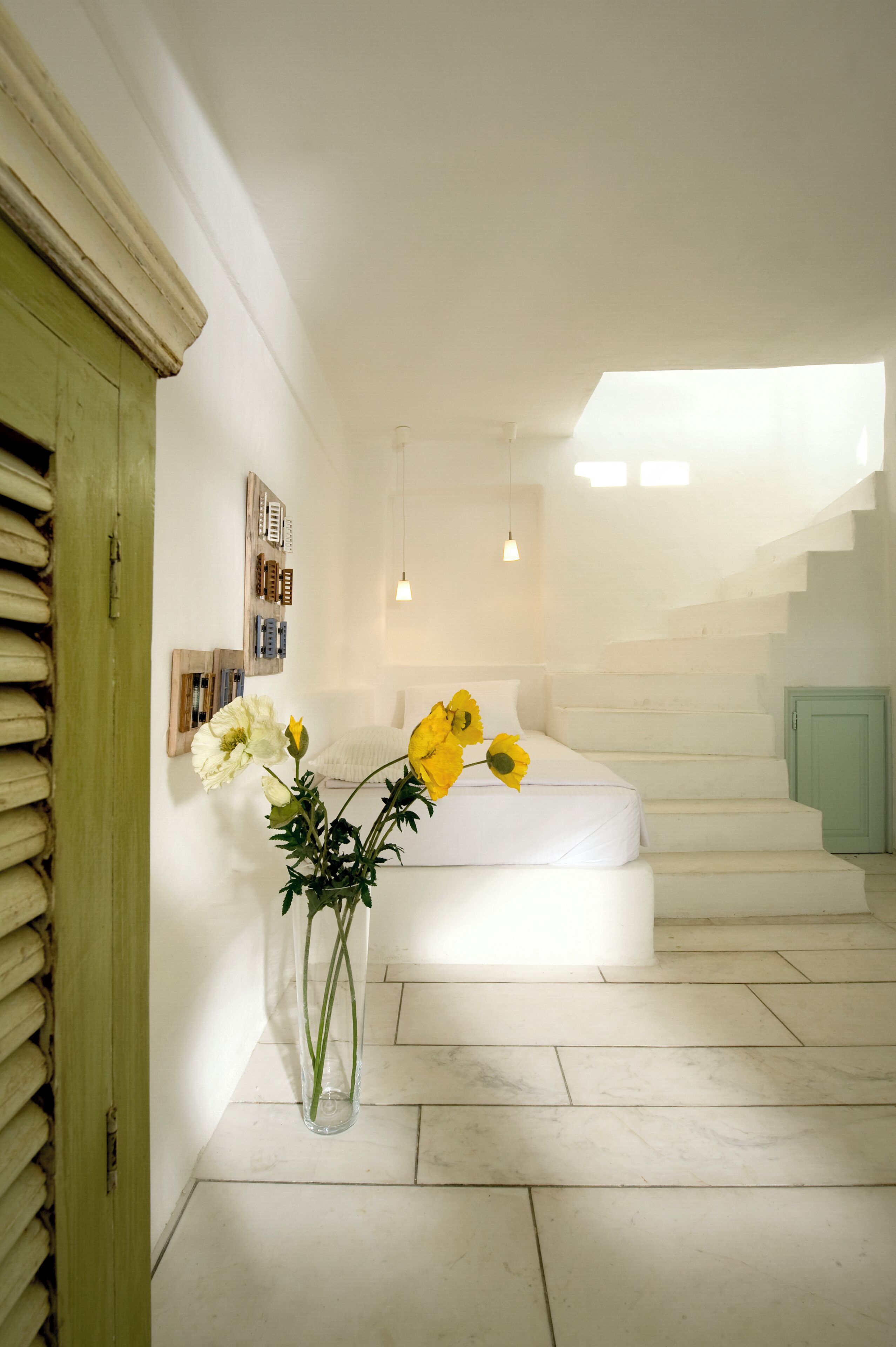 Un escalier menant à une chambre à coucher où se trouve un lit blanc et un vase rempli de fleurs jaunes.