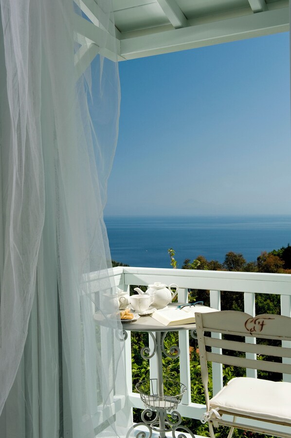 A balcony with a white chair, a table with a basket, and a view of the ocean. - Althea Boutique Hotel (Alonissos)