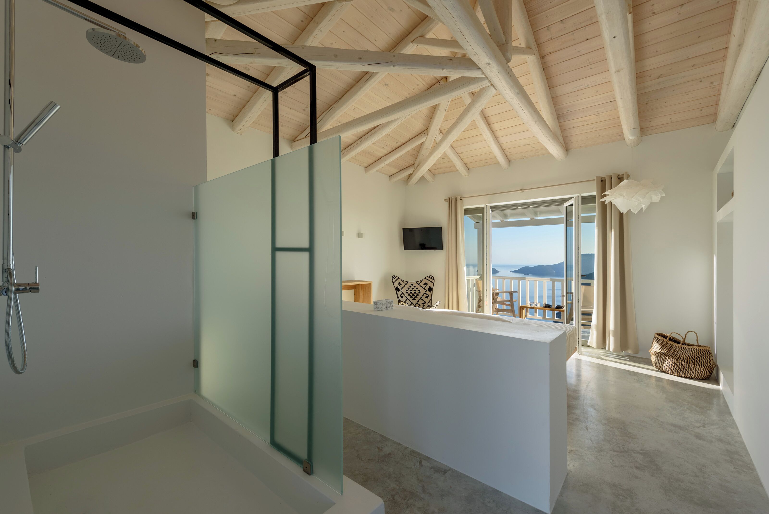 Et moderne badeværelse med en glasbrusekabine, træloft og havudsigt fra en balkon.