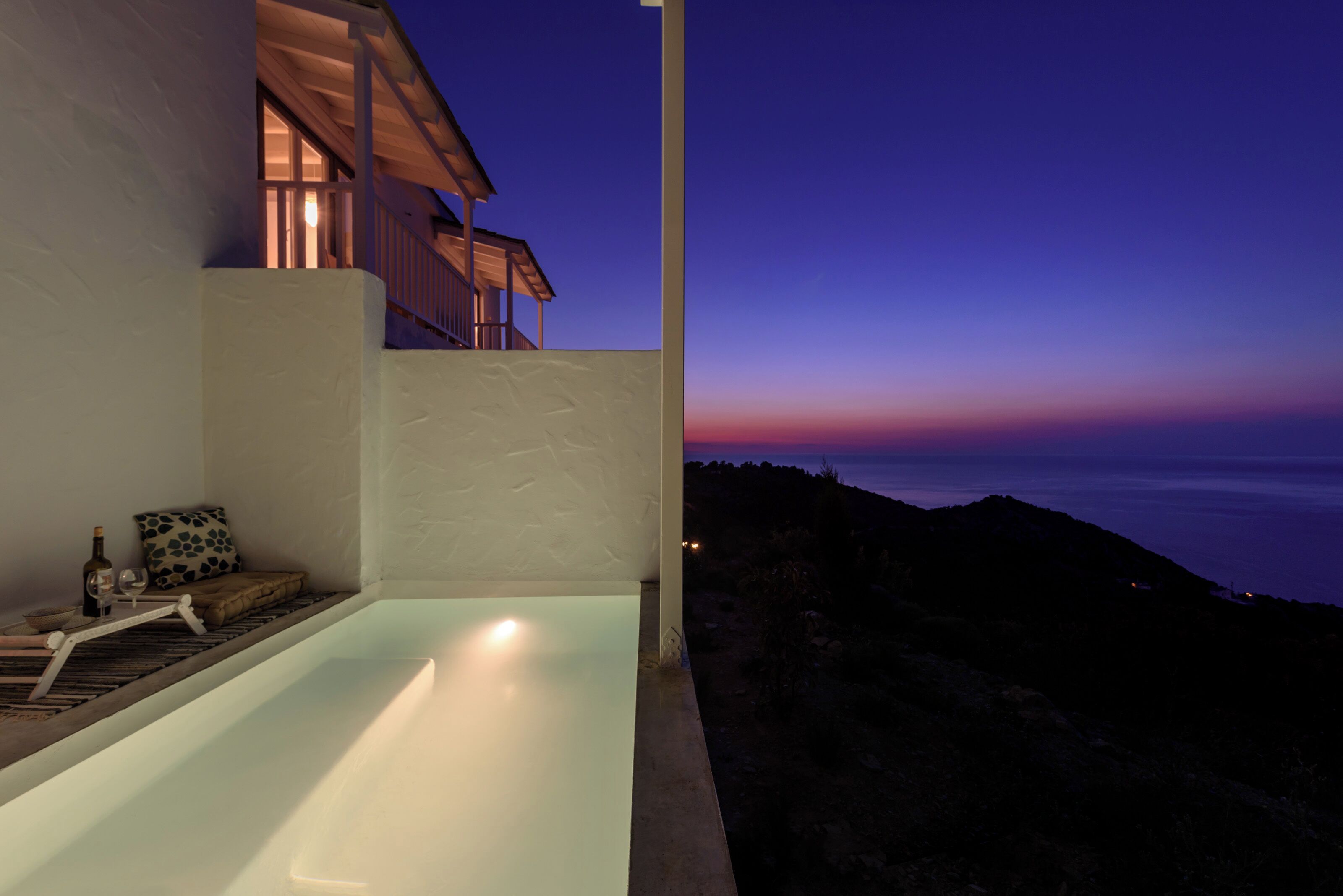 A modern outdoor bathtub area with a view of the ocean at dusk.