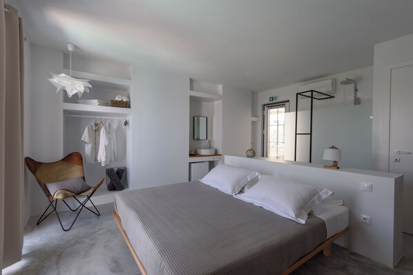 A modern bedroom with a bed, a chair, a vanity, and a large mirror. - Althea Boutique Hotel (Alonissos)
