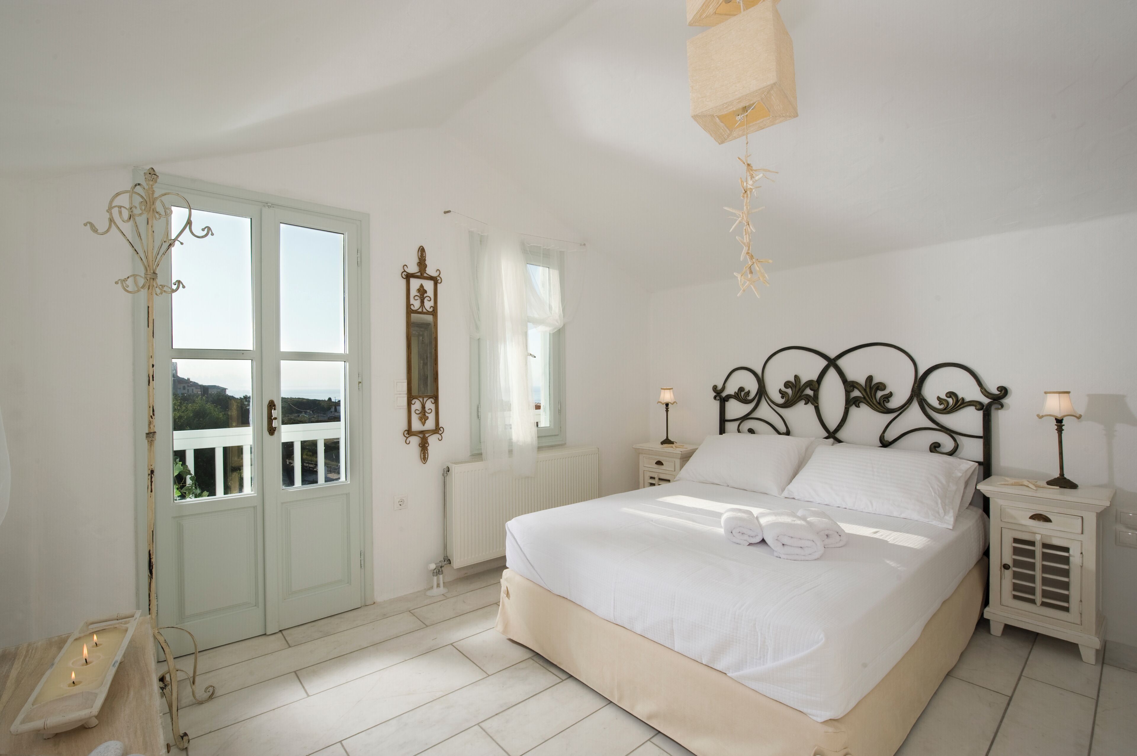 A bedroom with a bed, bedside tables, a mirror, and a window with a view.