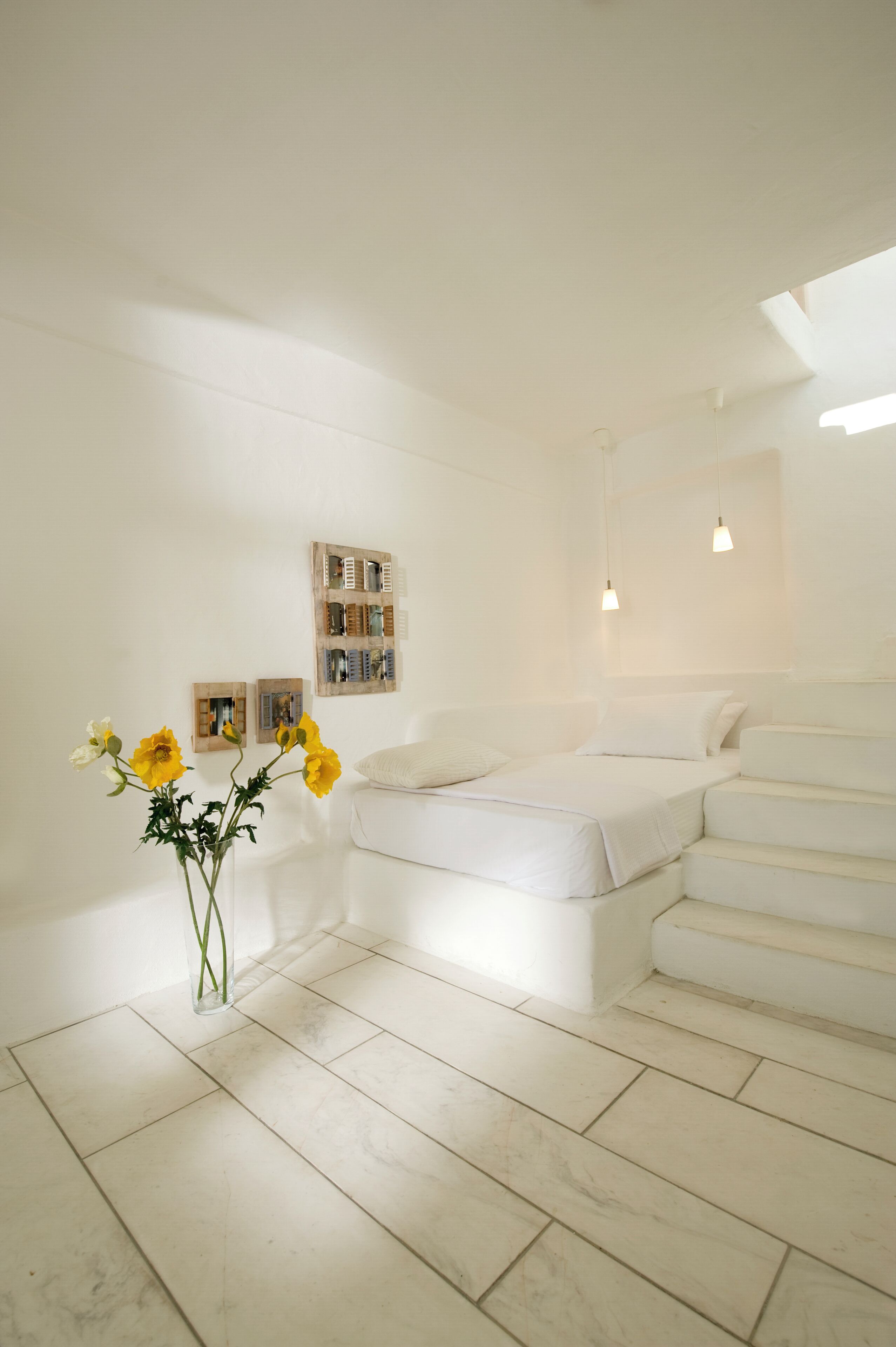 A minimalist bedroom with a bed, a white wardrobe, and a small table with a vase of flowers.