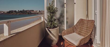 A balcony with a wicker chair, a potted plant, and a view of the sea.