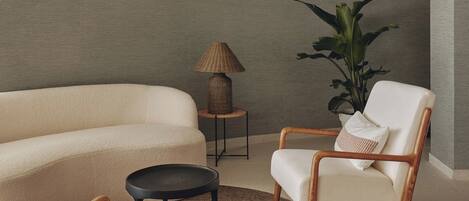 A modern living room with a beige sofa, two wooden armchairs, a small round table, and a floor lamp.