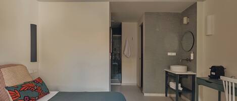 Un dormitorio con cama, escritorio, silla y baño con lavamanos y espejo.