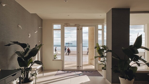 A modern hotel lobby with a view of the beach, large potted plants, and a reception desk. - Atlante Sanxenxo Boutique (Sanxenxo)