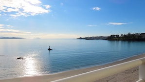 A calm sea with a small buoy in the water, a sandy beach, and a distant shoreline with buildings and trees. - Atlante Sanxenxo Boutique (Sanxenxo)