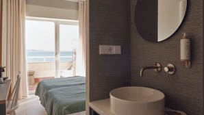 A hotel room with a bed, a round mirror, a sink, and a view of the sea through the balcony. - Atlante Sanxenxo Boutique (Sanxenxo)