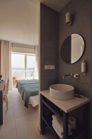 A hotel room with a bed, a round mirror, a sink, and a view of the sea through the balcony.