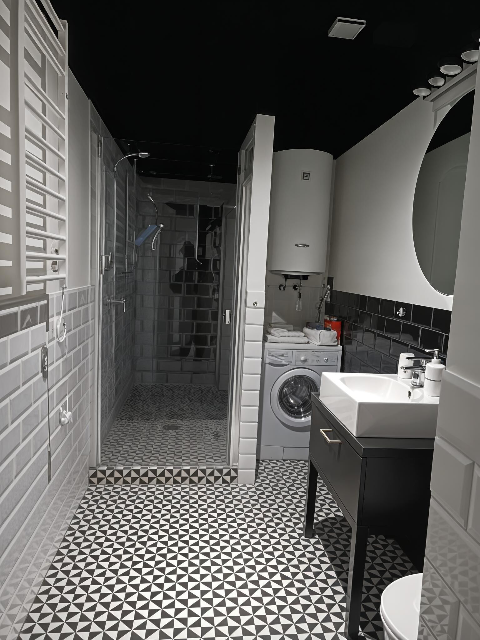Un baño moderno con piso de diseño geométrico, ducha con cerramiento de vidrio, lavadora integrada y un espejo grande sobre el lavamanos.