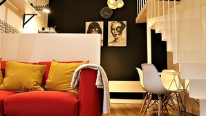 A modern living room with a red sofa, white and yellow cushions, a white chair, and a wooden floor. There are wall-mounted clocks and framed artwork above a black wall. - Cracow Fancy Brick #3 – Old Town (Kraków)