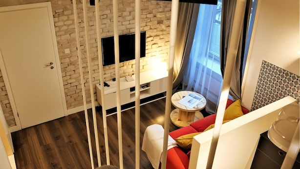 A modern room with a brick wall, a flat-screen TV, a small round table, and a red sofa. - Cracow Fancy Brick #3 – Old Town (Kraków)
