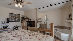 A bedroom with a bed, a ceiling fan, a nightstand, a dresser, a bathroom with a bathtub, a sink, and a mirror.