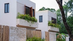 A modern multi-story building with balconies, stone and wooden walls, and lush greenery. - Jungle Villa Oasis, large private pool & Starlink (Tulum)