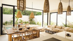 A modern living room with a large window, a dining area with a wooden table and chairs, and a sofa. - Jungle Villa Oasis, large private pool & Starlink (Tulum)