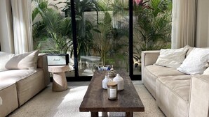 A modern living room with a beige sofa, a wooden coffee table, and a glass door leading to a balcony with tropical plants. - Jungle Villa Oasis, large private pool & Starlink (Tulum)