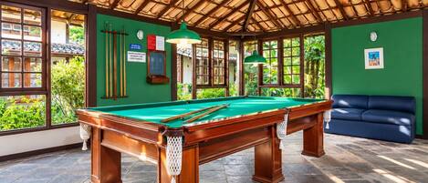 A pool table in a room with a green wall, a blue sofa, and a thatched roof ceiling.