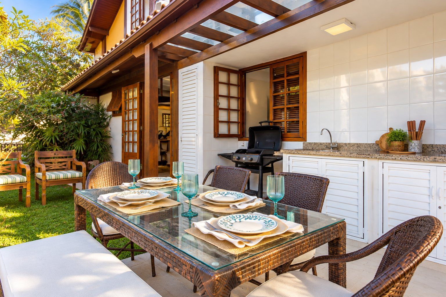 An outdoor dining area with wicker furniture, a glass table, and a grill.