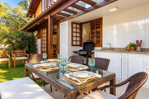 An outdoor dining area with wicker furniture, a glass table, and a grill. - Bz16 Casa com Churrasqueira privativa (Buzios)