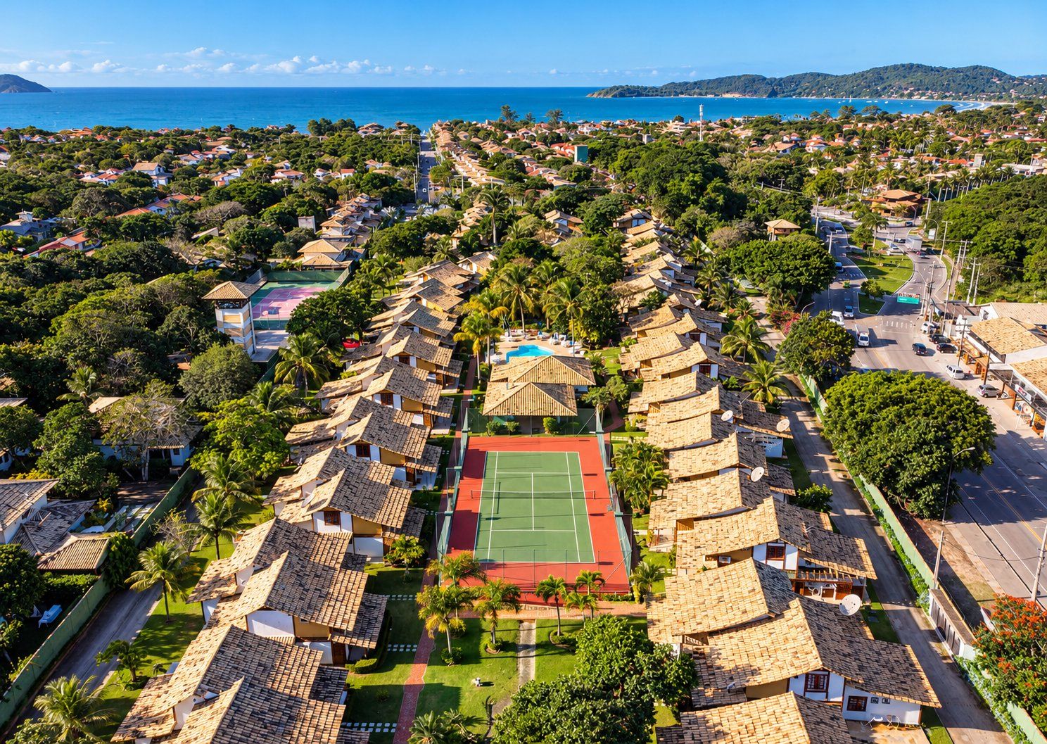 A coastal residential area with houses, a tennis court, and a beach in the background.