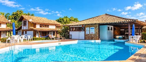 A swimming pool with lounge chairs and a covered area, surrounded by buildings with tiled roofs.