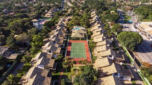 Vista aérea de una zona residencial con casas, una cancha de tenis y vistas al mar.
