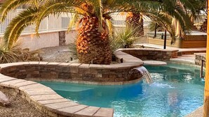 Ein Pool mit Steinrand, einer Palme und einem Wasserfall.