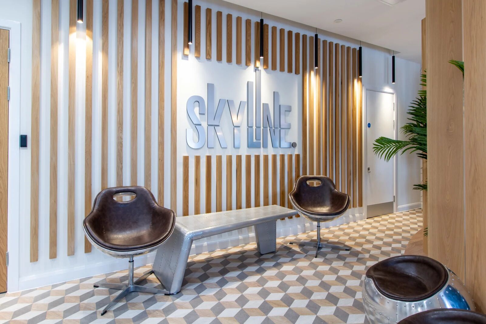 A reception area with a modern design, featuring a bench and two chairs, a patterned floor, and a wall with vertical wooden slats and a 'SKYLINE' sign.