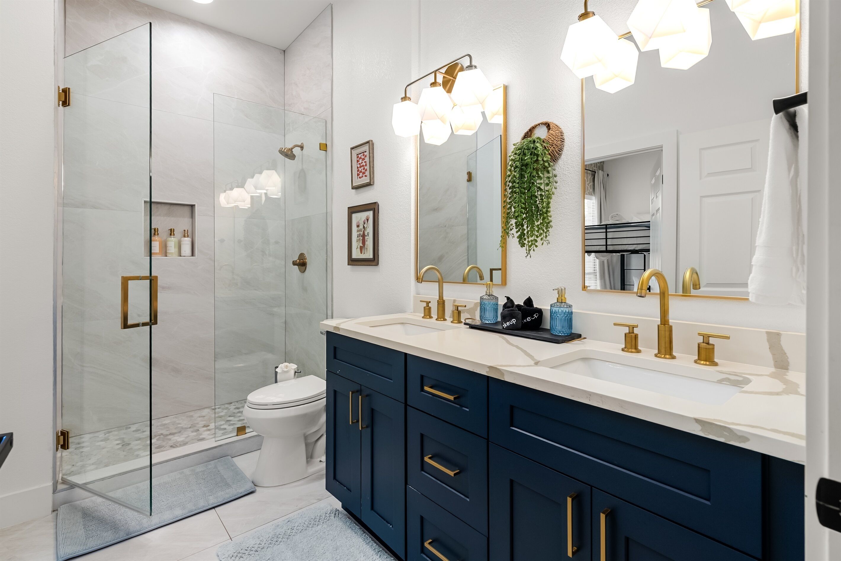 A modern bathroom with a glass shower enclosure, a white toilet, and a vanity with dark blue cabinets and gold fixtures.