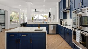 A modern kitchen with dark blue cabinets, stainless steel appliances, and a large island with a sink.