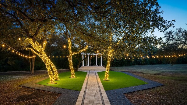 A paved pathway leading to a gazebo with string lights and a lawn area.