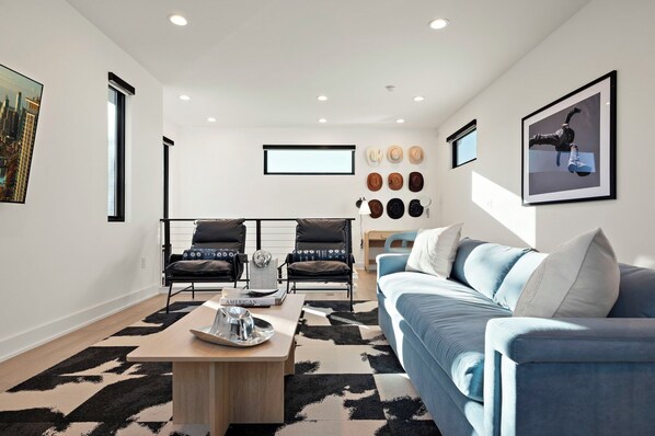 A modern living room with a blue sofa, two armchairs, a coffee table, and a wall-mounted hat display.
