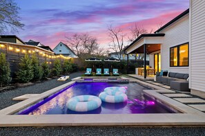 A backyard with a swimming pool, lounge chairs, and a covered patio area.
