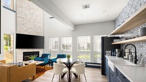 Eine moderne Küche mit Einbauherd, eine Essecke mit rundem Tisch und Stühlen sowie ein Wohnzimmer mit Kamin und Sofas.