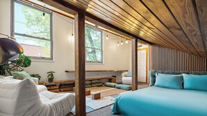 A cozy attic bedroom with a sloped ceiling, wooden beams, a bed, a sofa, and a desk. - Haven de Luz: A Tranquil Retreat ~ Pool|Spa|Sauna (Austin)