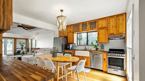 A modern kitchen with wooden cabinets, a central island, and a dining area with white chairs. - Haven de Luz: A Tranquil Retreat ~ Pool|Spa|Sauna (Austin)