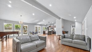 Un salon spacieux avec deux canapés en cuir gris, un piano en bois et un coin repas comprenant une table et des chaises.
