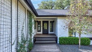 Une maison moderne avec une terrasse en bois, une porte d’entrée noire et un arbre dans le jardin.