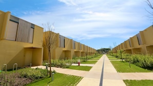 A row of modern, beige-colored buildings with a central pathway flanked by greenery and small trees. - Villa Essence by Clever Details, private pool, walk distance to the marina (Quarteira)