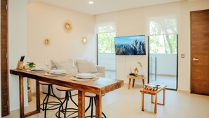 Een moderne woonkamer met een houten eettafel, een bank en een aan de muur bevestigde televisie.