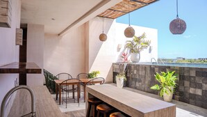 Een modern buitenmeederegebied met een houten tafel en stoelen, een bar en hangende rieten lampen.