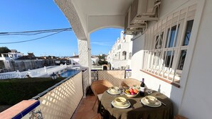 A balcony with wicker chairs, a table set for dining, and a view of a swimming pool and buildings in the background. - Verano Azul 72 (Nerja)