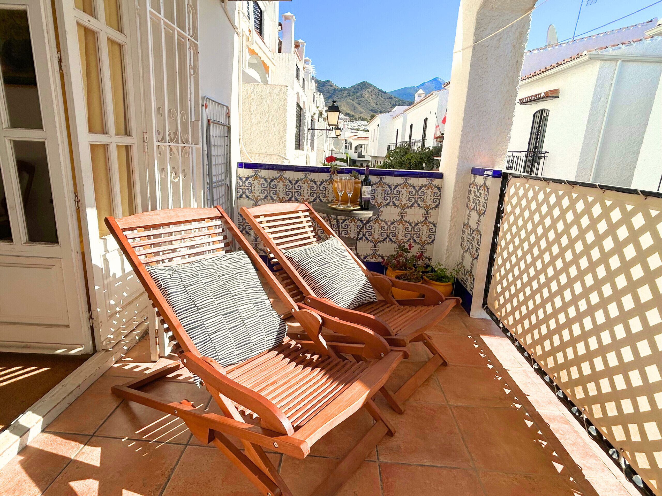 A terrace with wooden lounge chairs and a tiled wall with a decorative pattern.