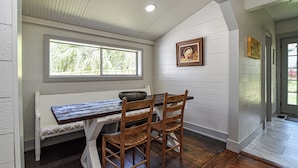 A dining area with a wooden table and chairs, a bench, and a window with a view of greenery. - The Spruce House Cozy Home in Swannanoa (Swannanoa)